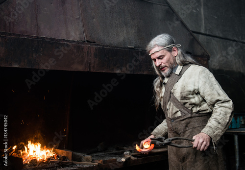 Gray-haired smith forges detail in the smithy