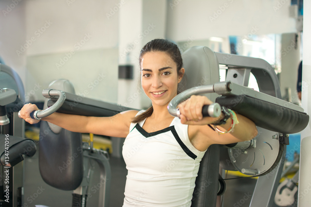 Fototapeta premium Young woman doing exercises on chest press gym machine in fitness center.