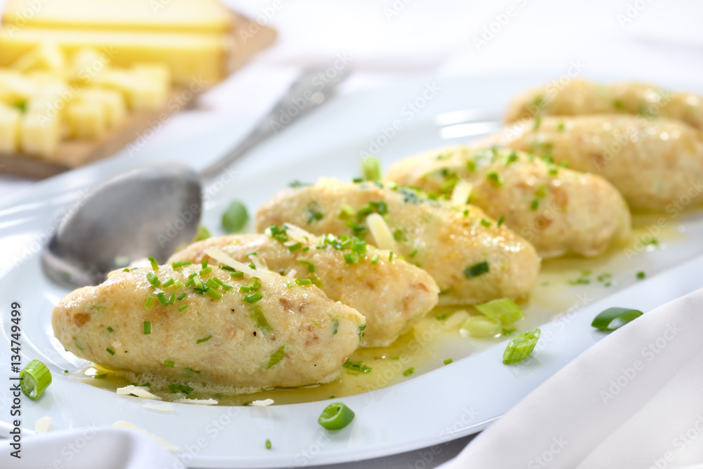 Deftige Südtiroler Kasnocken mit gebräunter Butter und Parmesen auf weißer Platte serviert - South Tyrolean cheese dumplings made of white bread and mountain cheese, served with melted butter