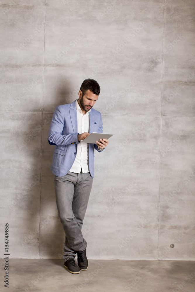 Young man with tablet by the grey wall
