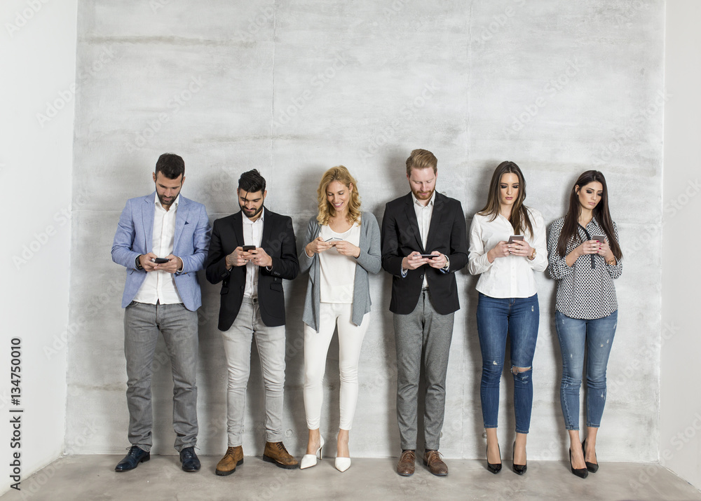 Obraz premium Young business people with mobile phone standing by the wall