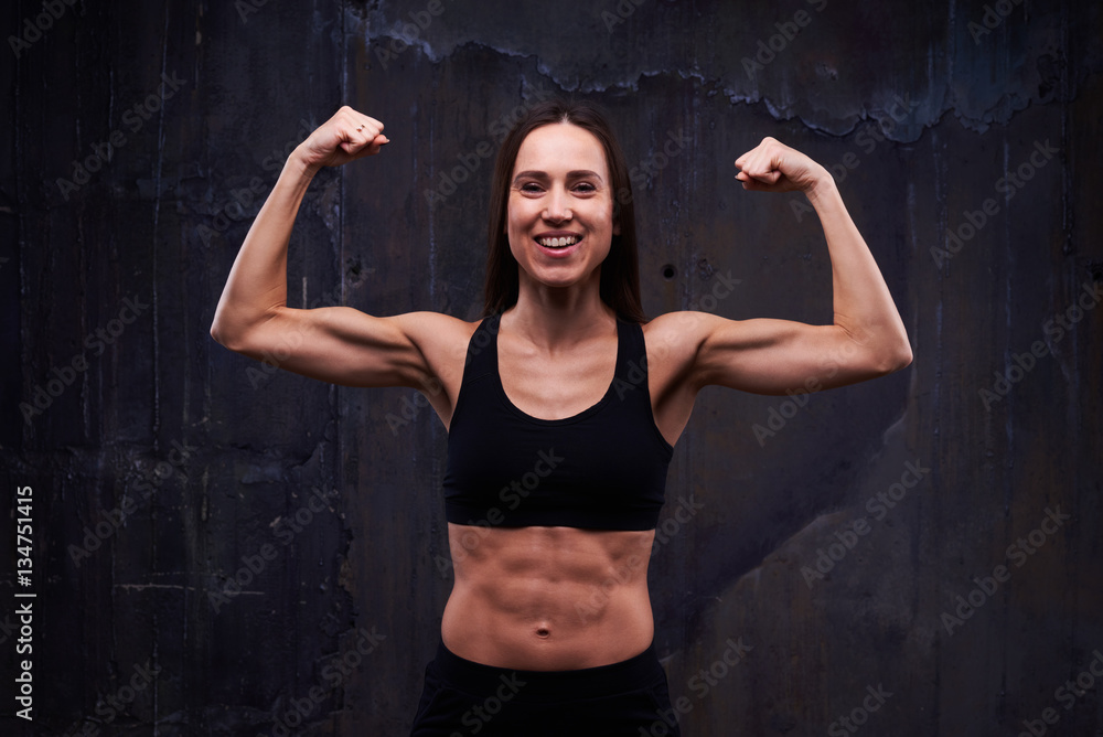 Fototapeta premium Happy fitness model showing trained biceps isolated against blac