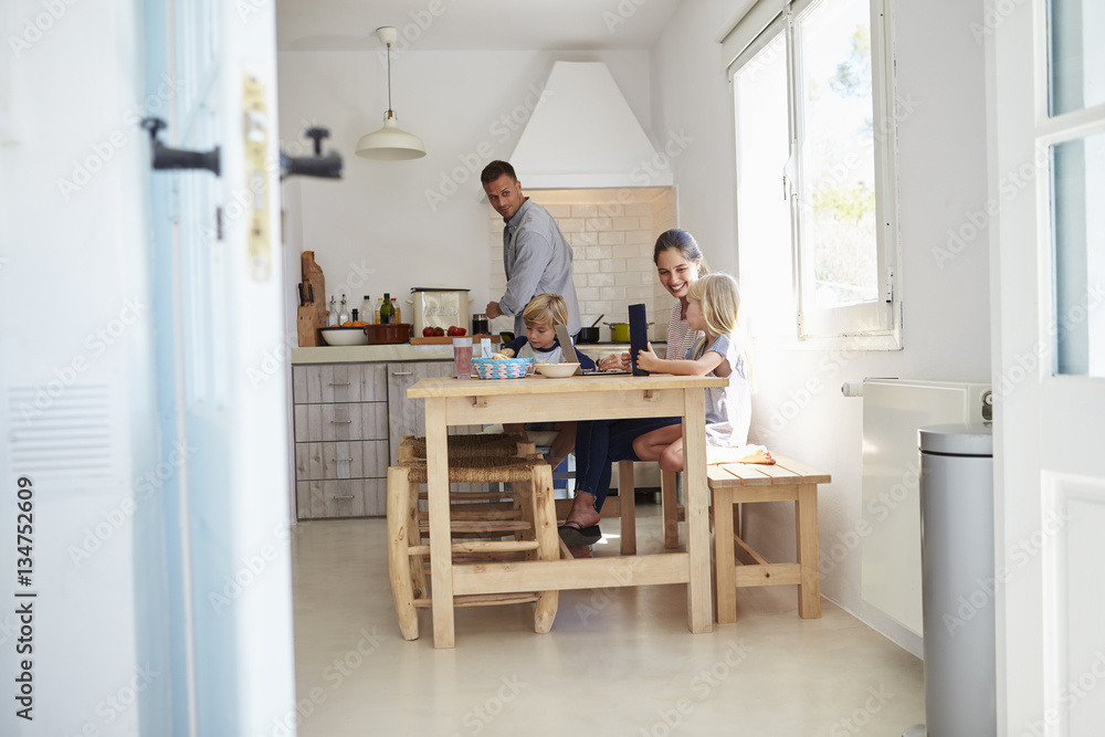 Fototapeta premium Kids at kitchen table with mum, dad cooks, view from doorway