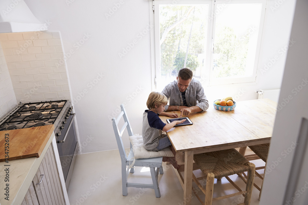 Dad and son use tablet in kitchen, elevated view from doorway Dad and son use tablet in kitchen, elevated view from doorway