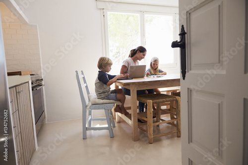 Mum and two kids working at kitchen table, seen from doorway