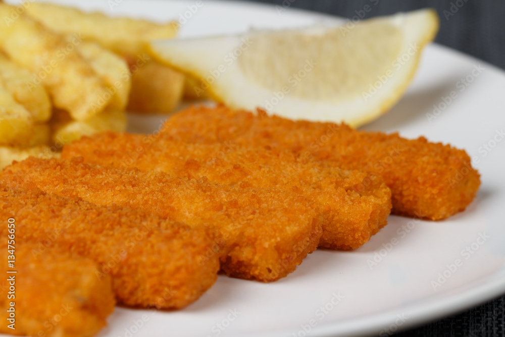 Fish fingers sticks with lemon on white plate, closeup, low focus Fish fingers sticks with lemon on white plate, closeup, low focus