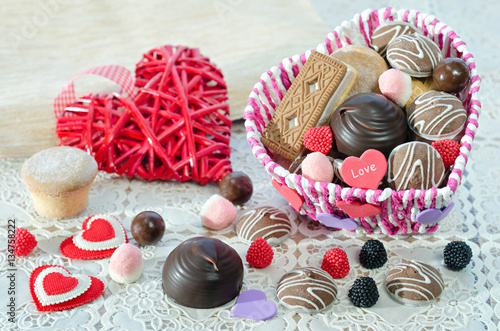 Basket with sweets and biscuits on the table, a decorative Valentines day hearts and sweets scattered. Selective focus.