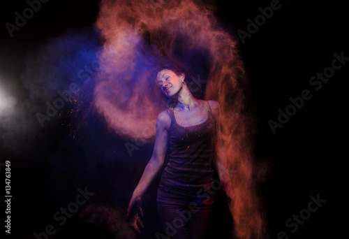 Young girl in a dark shirt and jeans in the studio light beam. She left orange blue trace of powder paint with the help of hair. This track reminds flame.