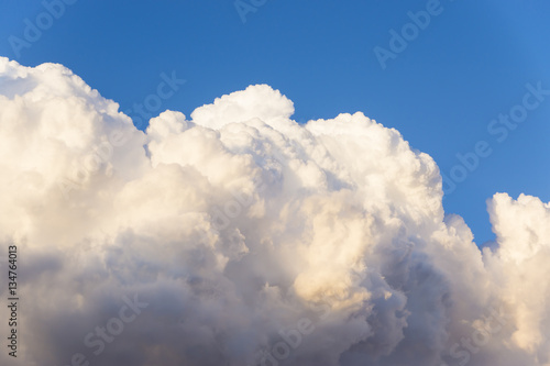 Part of a large cumulus clouds illuminated by the sun on a background of a piece of clear blue sky © morelena