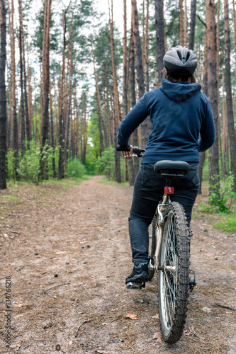 Girl on bicycle rides at the road in coniferous forest