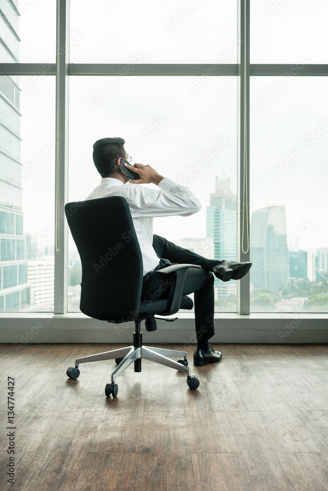Rear view of businessman talking on phone while sitting down Rear view of businessman talking on phone while sitting down