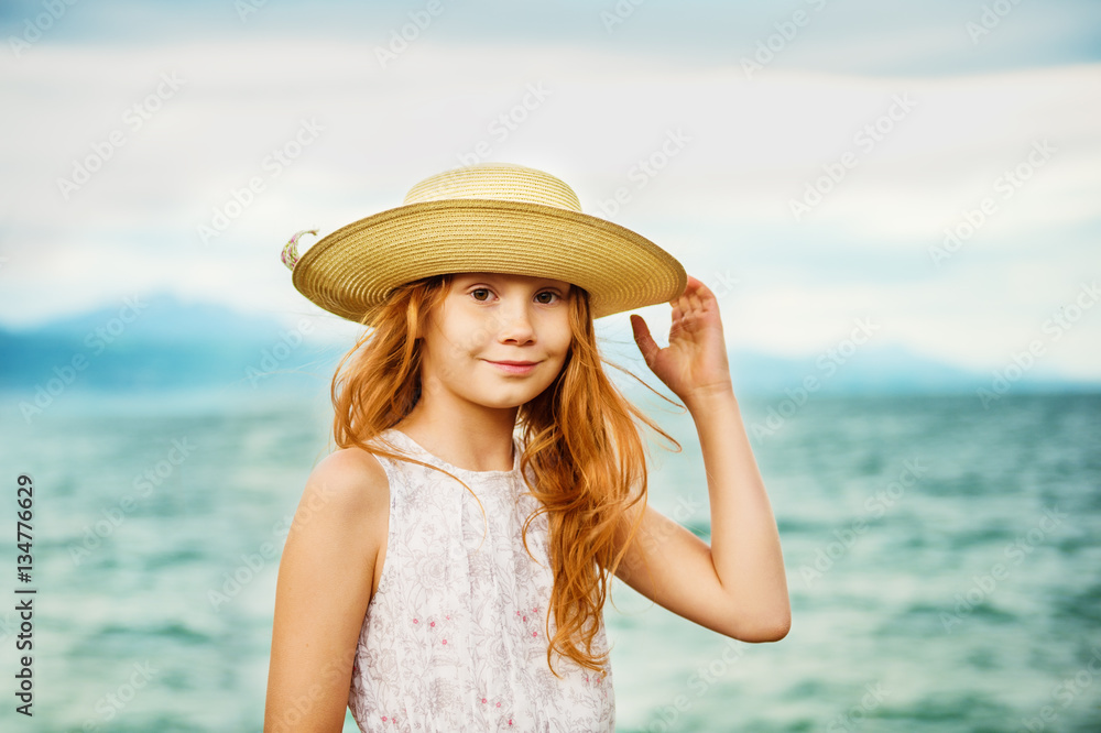 Pretty little girl with long red hair playing by the lake on a very windy day, wearing big hat Pretty little girl with long red hair playing by the lake on a very windy day, wearing big hat