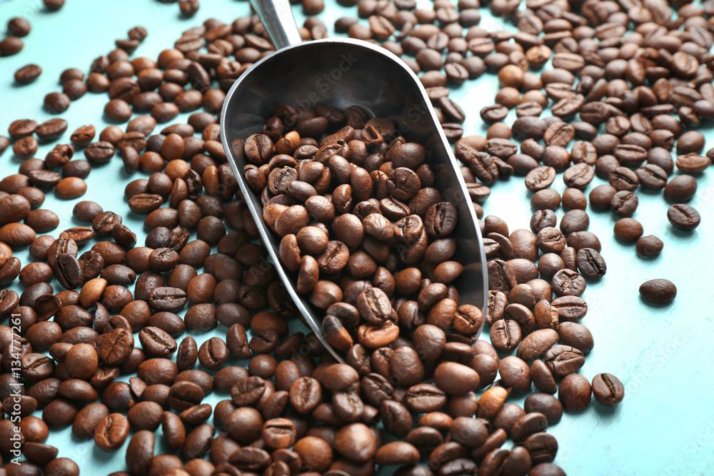 Fototapeta premium Roasted coffee beans and metal scoop on wooden table closeup