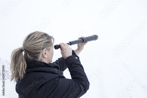 Woman looks with telescope in snowy landscape