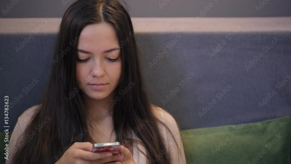 Close up view of woman talking and working with cell phone. Sitting on sofa young and beautiful female is using mobile device typing, messaging or creating some text surfing the internet looking Close up view of woman talking and working with cell phone. Sitting on sofa young and beautiful female is using mobile device typing, messaging or creating some text surfing the internet looking