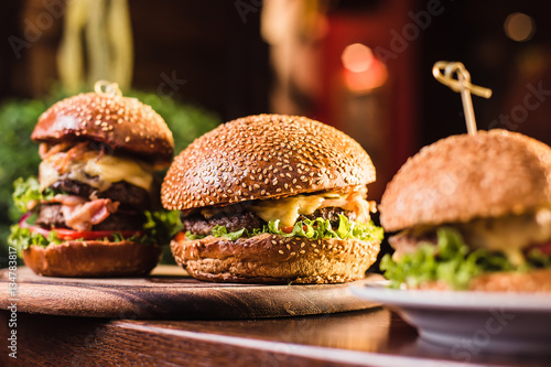 Three juicy tasty burger on the white plate on a dark background © artem_goncharov