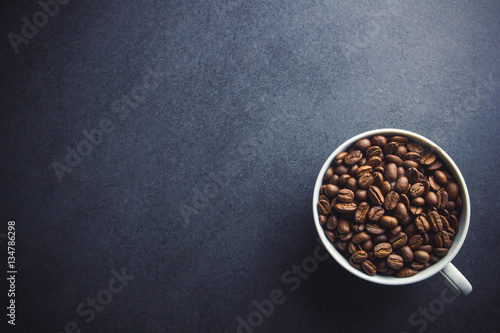 White coffee cup filled with coffee seeds on black surface background.
