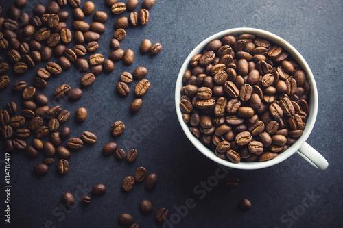 White coffee cup filled with coffee seeds on black surface background.