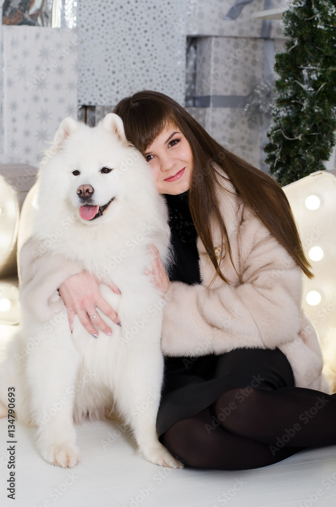 Attractive girl in a fur coat hugging a fluffy snow white Samoyed Attractive girl in a fur coat hugging a fluffy snow white Samoyed