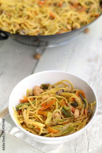 Noodles with chicken and various vegetables, prepared in wok. Served on white rustic table. Selective focus. 
