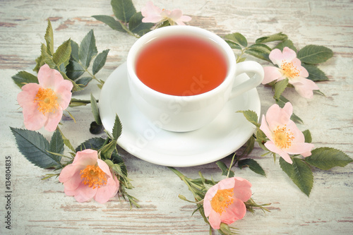 Vintage photo, Cup of tea and wild rose flower on old rustic wooden background