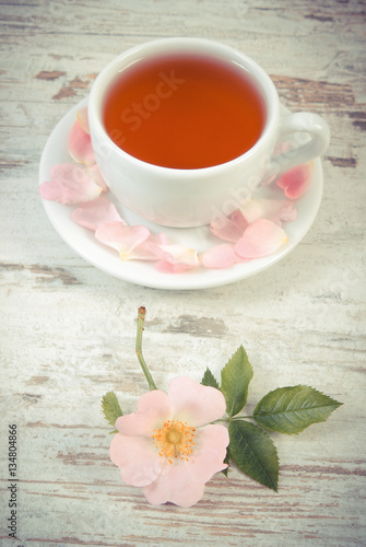 Vintage photo  Cup of tea and wild rose flower on old rustic wooden background