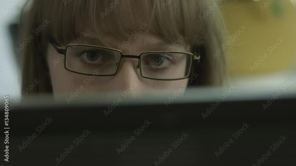 Ungraded: Girl with eyeglasses looks into the computer monitor. When she distracted she nods to someone behind the monitor. Ungraded: Girl with eyeglasses looks into the computer monitor. When she distracted she nods to someone behind the monitor.
