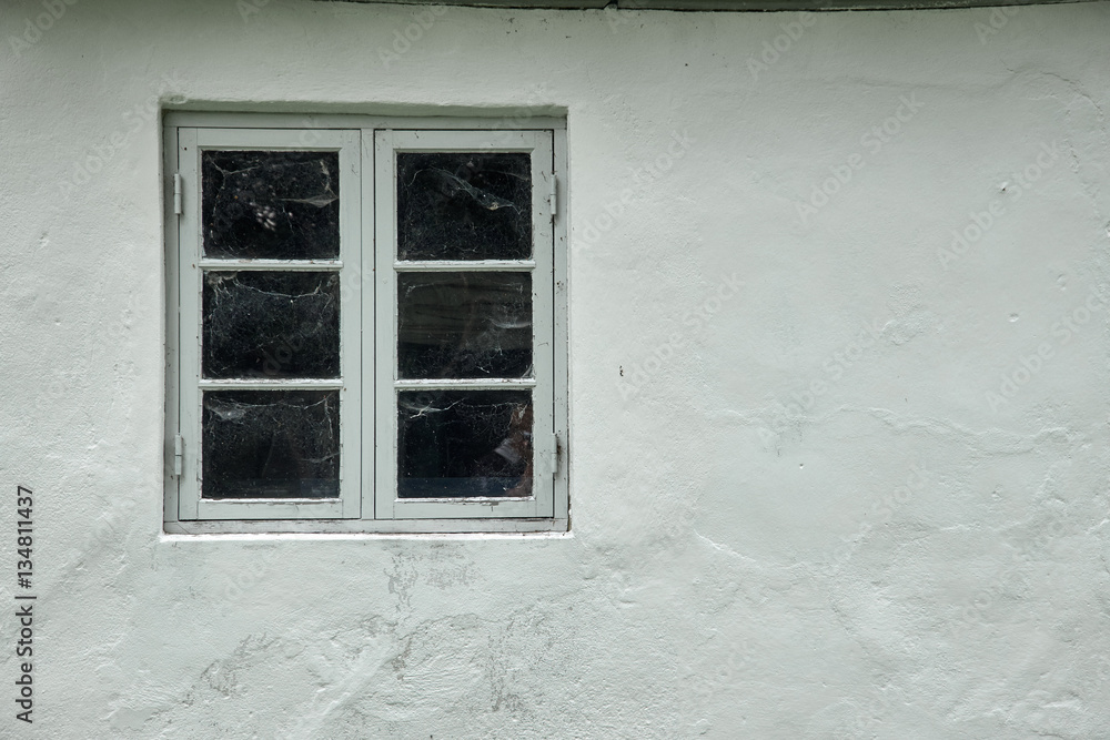 Fototapeta premium One gray wood colonial style window, with spider web on the inside, fastened in a white painted plastered facade