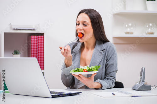 Young businesswoman is eating salad in her office.