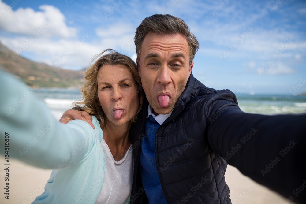 Mature couple sticking out tongue while taking selfie - obrazy, fototapety, plakaty 
