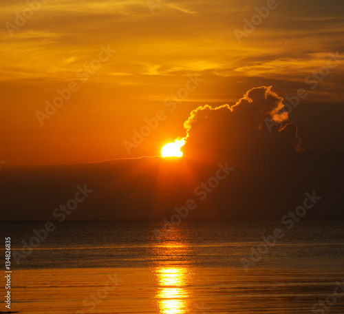 Sun in the clouds above the seascape with mirror reflection