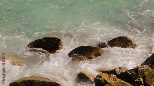 Beautiful white bubbles created on the beach by ocean waves on seashore. The ocean waves hit the rocks on the beach.