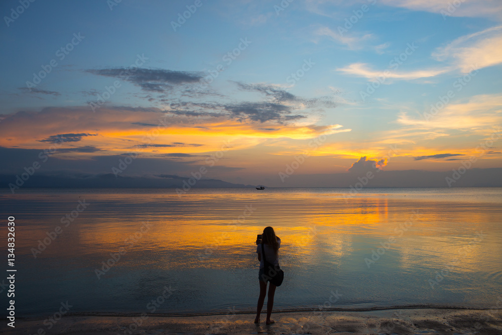 Woman stay on sand beach and try to do mobile photo at the evening landscape with sea and clouds