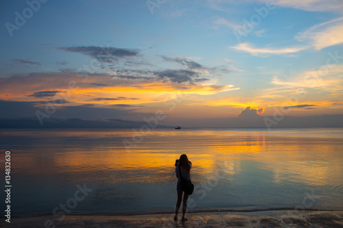 Woman stay on sand beach and try to do mobile photo at the evening landscape with sea and clouds
