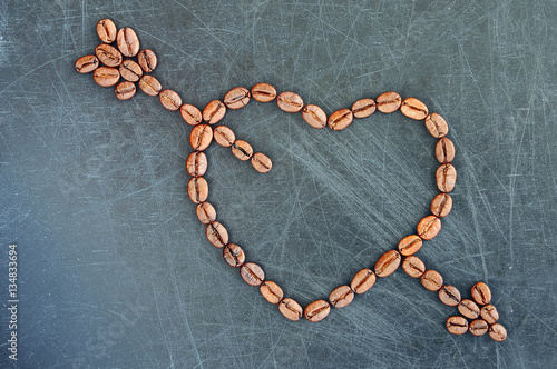 Heart with cupid arrow made of coffee beans on a dark background.