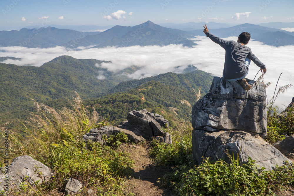 Obraz premium man sitting on the cliff and looking at the valley and mountains in the daylight