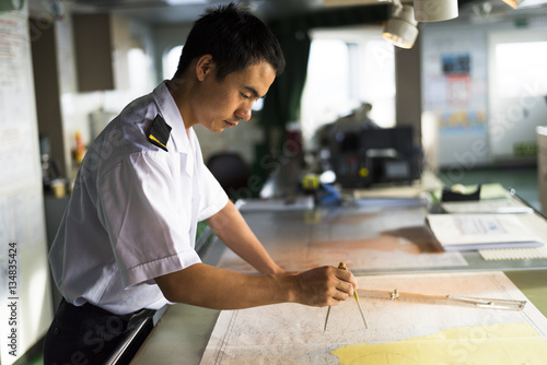 Young Chinese Navigator Doing Chartwork on Bridge photo