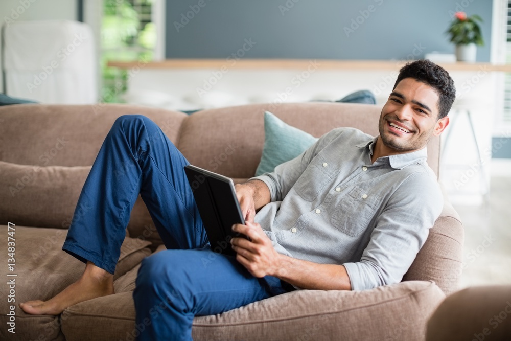 Man lying on sofa and using tablet in living room Man lying on sofa and using tablet in living room