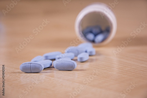 Pills pouring out of a bottle. Close up of medication. Pharmacy prescription drugs on a wooden table. Focus on the pills.