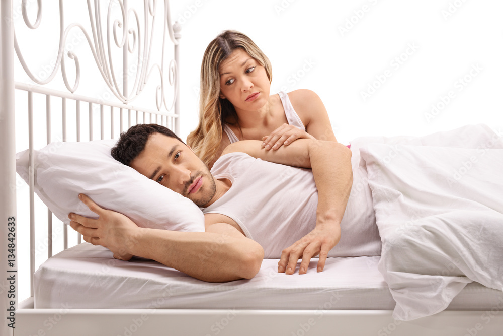 Unhappy man lying in bed with concerned woman comforting him Unhappy man lying in bed with concerned woman comforting him
