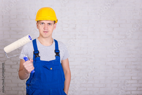young man painter in workwear with roller paintbrush over white