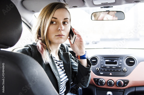 Beautiful young attractive woman sitting in driver seat in the car looking back and holding mobile phone