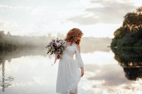 The bride with a bouquet on beautiful large lake background at sunset. Rustic Wedding