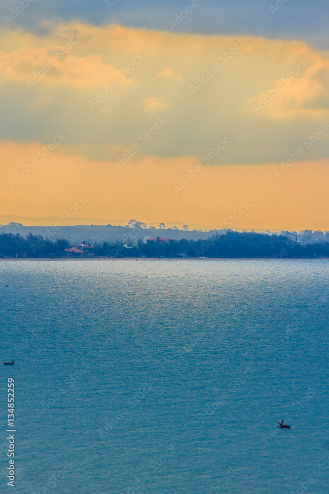 Beautiful sunrise over the sea in the morning on cloudy day that sun beams break through the clouds. Sun beaming through clouds with urban landscape, if you zoom in will see the small fishing boats.