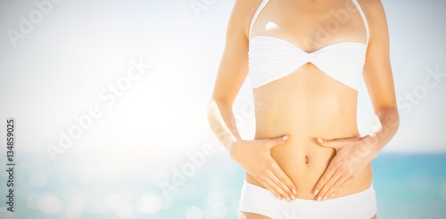 Midsection of woman in bikini touching her belly