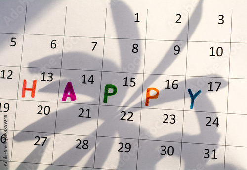 On the calendar sheet is written the word "happy." On the calendar page the shadow of the leaves of the plant. 