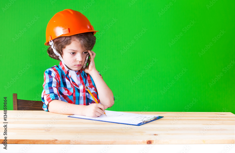 Serious little foreman wrote in pencil in a notebook with a phone in his hand. Close-up. Green background. Serious little foreman wrote in pencil in a notebook with a phone in his hand. Close-up. Green background.