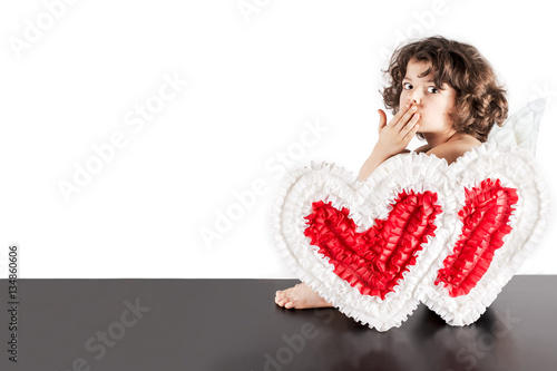 Little curly angel sitting on a black floor half-turned and sent a kiss to the camera. Close-up. White background. © kravik93