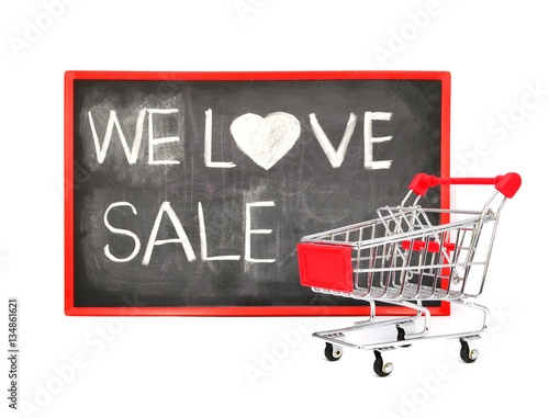 Shopping cart with chalk written word "We Love Sale" on black bo