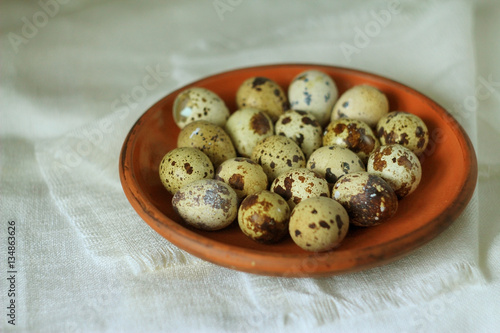  Quail eggs lie in a ceramic dish on a table. There is  a white linen tablecloth On the table